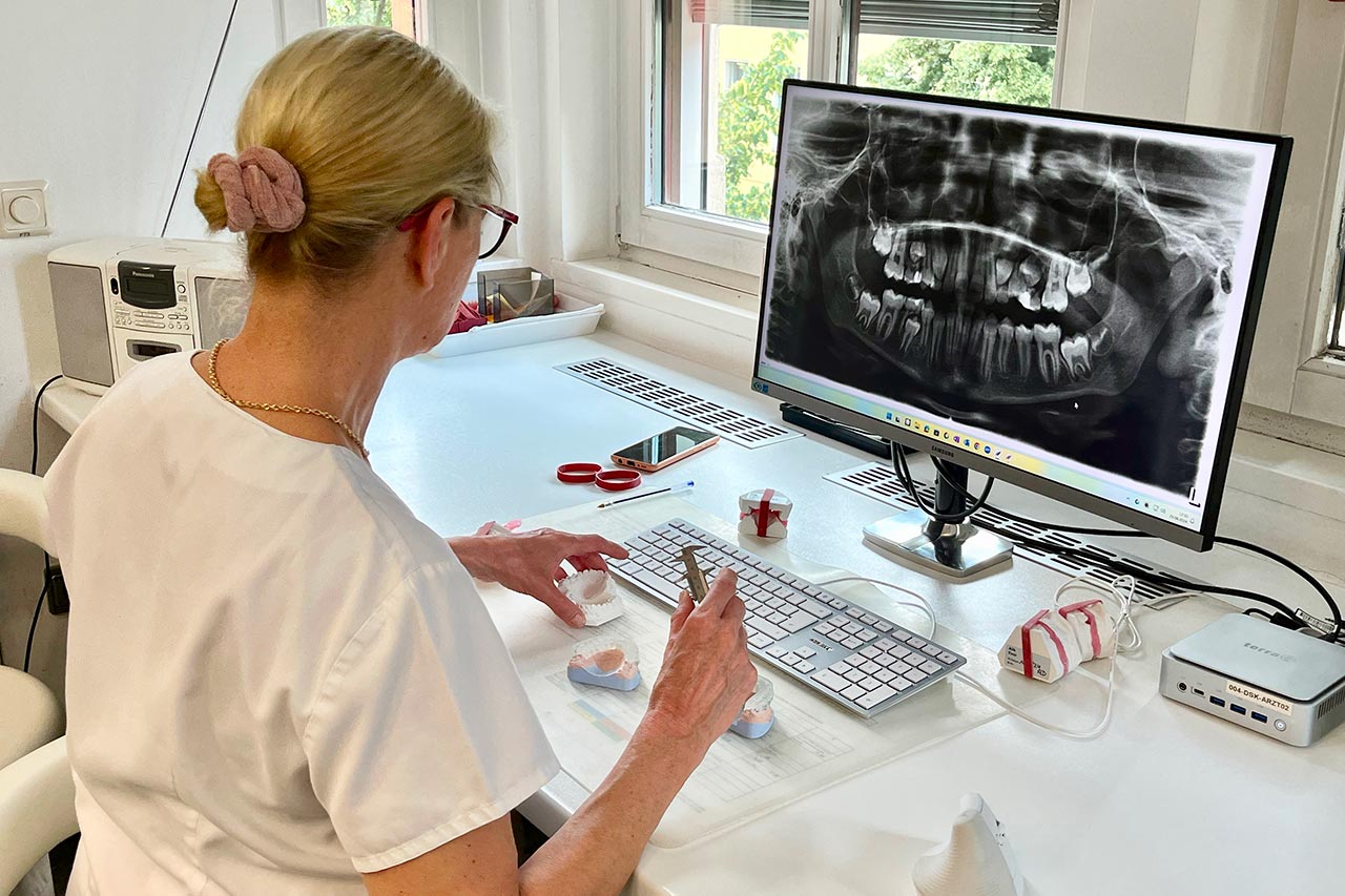 Mitarbeiterin plant anhand eines Röntgenbildes auf dem Monitor und einigen Gips-Gebissmodellen eine Behandlung